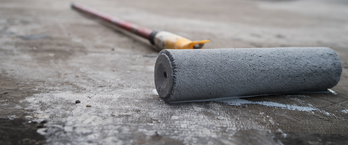 A paint roller laying on the concrete.